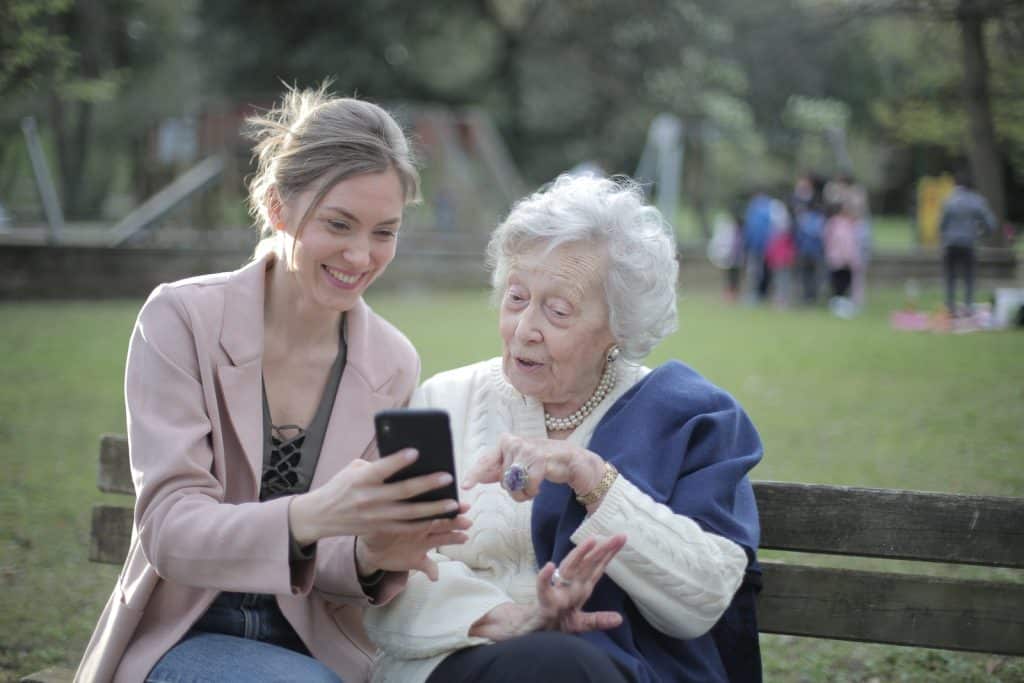 Parents ravis, assis ensemble sur un banc en bois dans un parc et naviguant sur leur téléphone portable tout en apprenant à l'utiliser